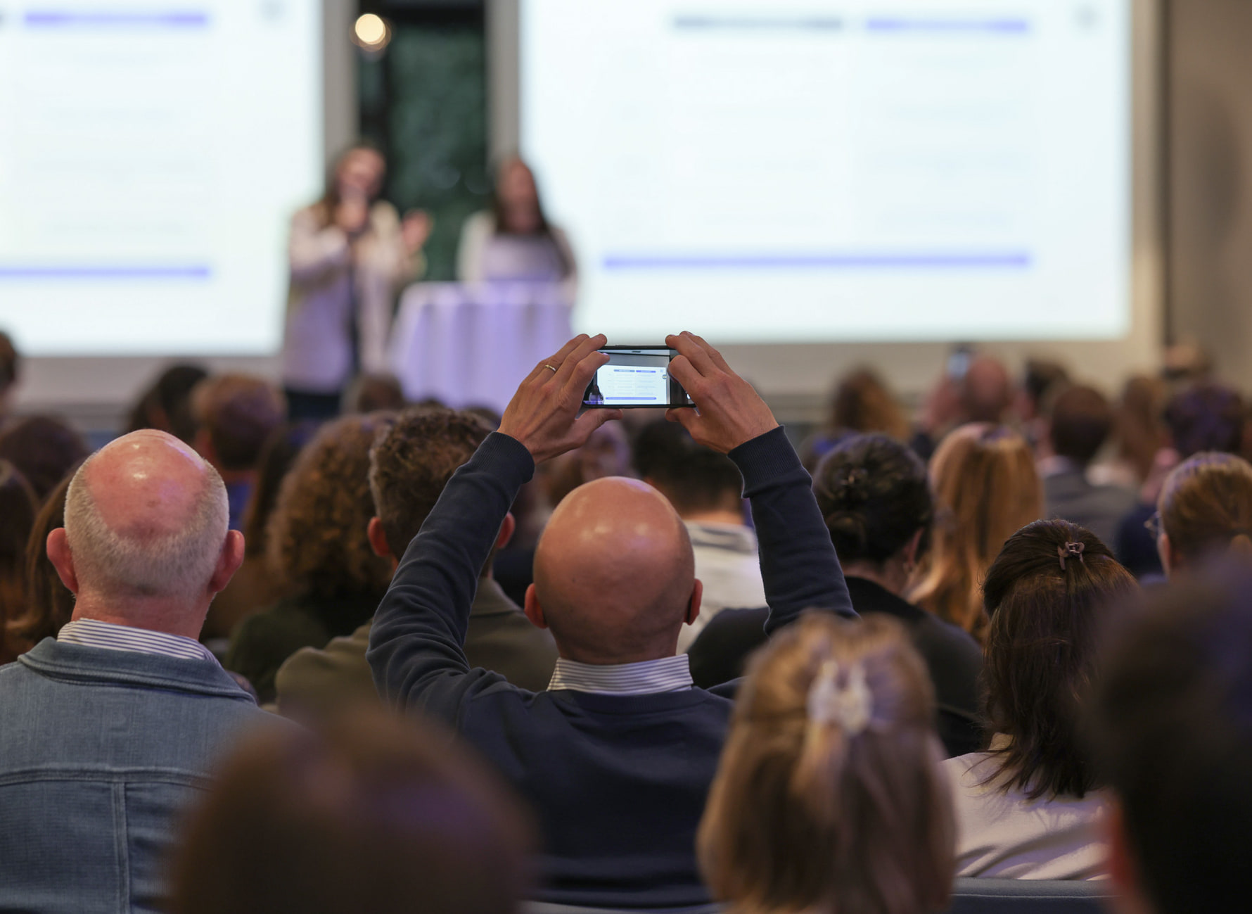 Le public de dos, un téléphone levé pour photographier l’écran.