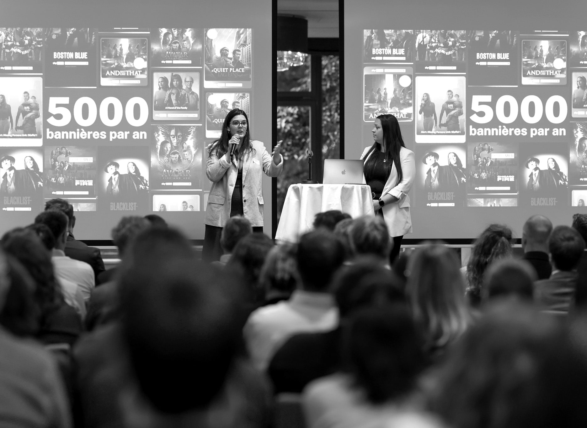 Photo en noir et blanc d’une intervention devant un écran annonçant 5000 bannières par an.