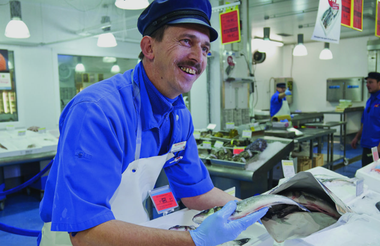 Poissonnier souriant présentant un poisson frais derrière l’étal de la poissonnerie