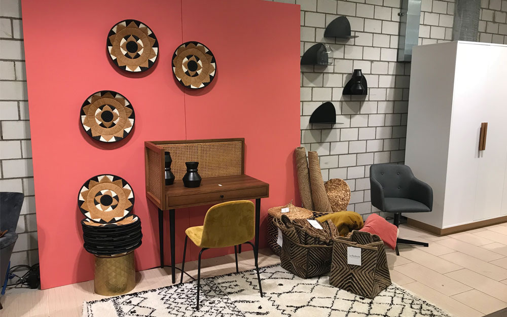 Coin bureau décoré : bureau en bois et cannage, chaise moutarde, paniers tressés et assiettes murales sur fond corail