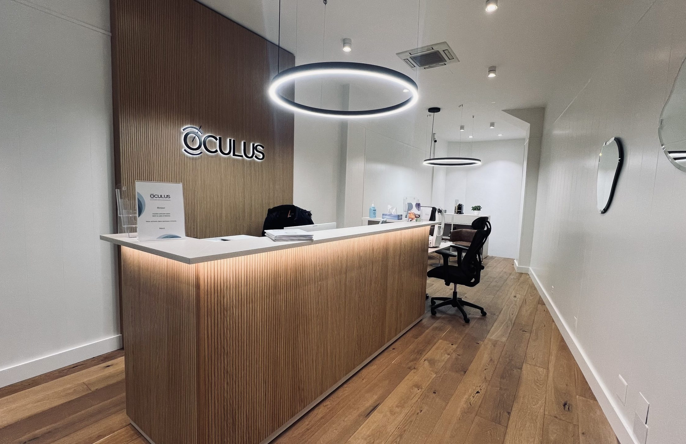 Accueil d’une clinique Oculus, comptoir en bois éclairé et logo au mur