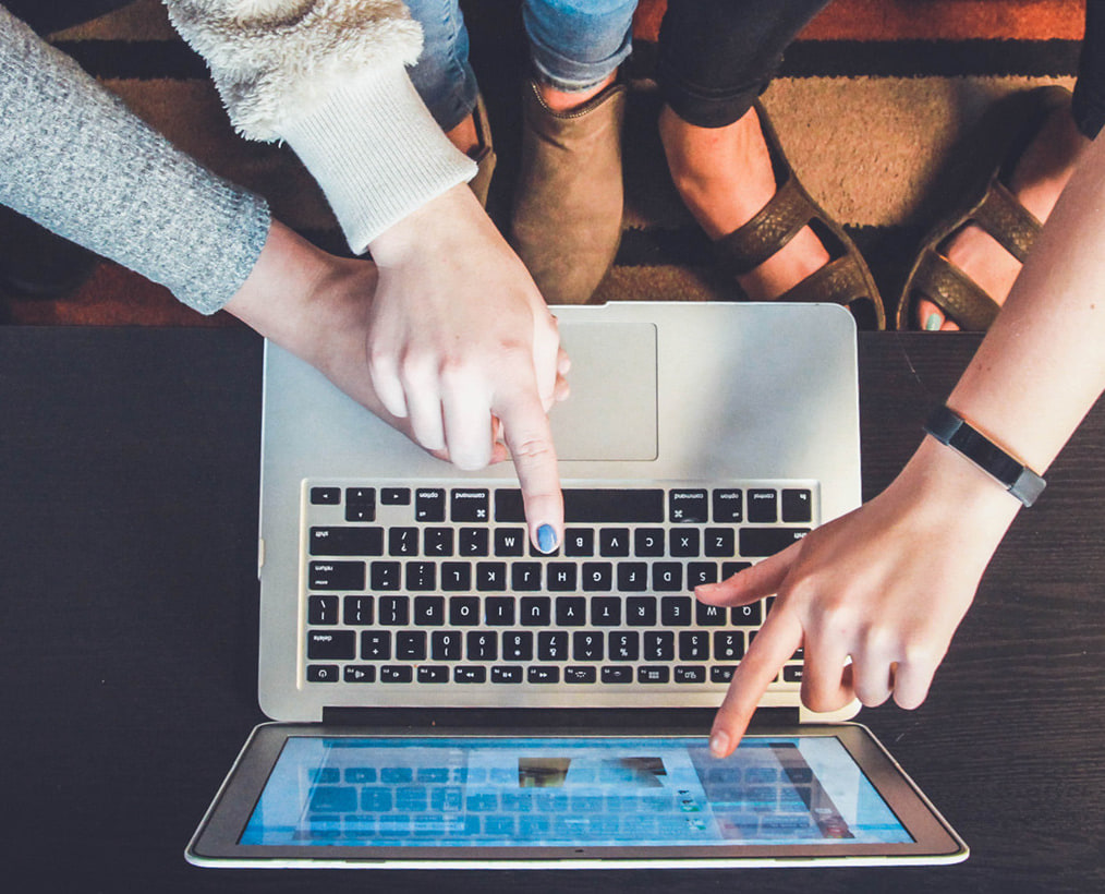 Vu de dessus, trois paires de mains autour d’un ordinateur portable et d’une tablette, un doigt sur le clavier.