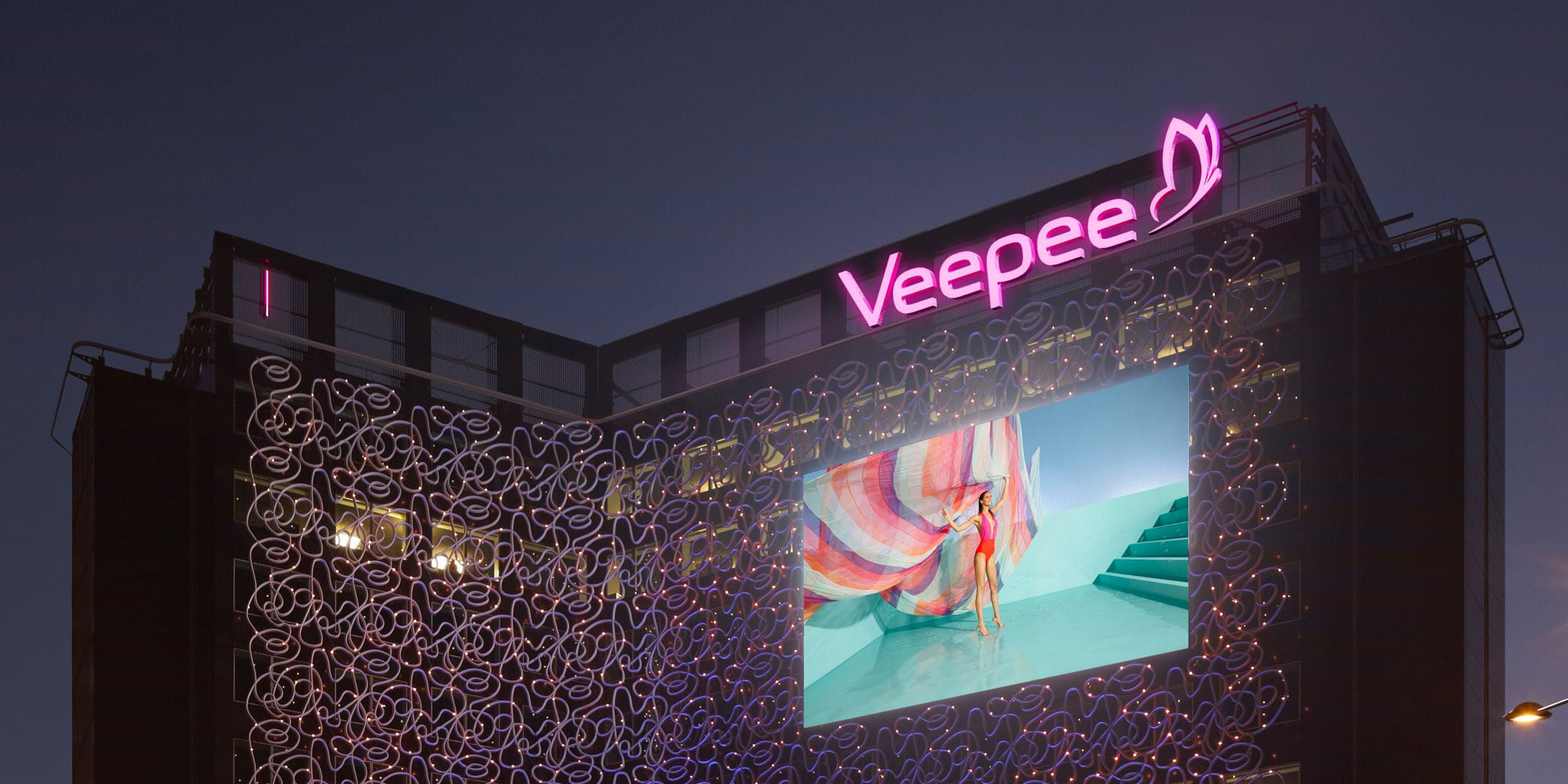 Siège de Veepee de nuit, enseigne lumineuse rose et écran géant sur la façade