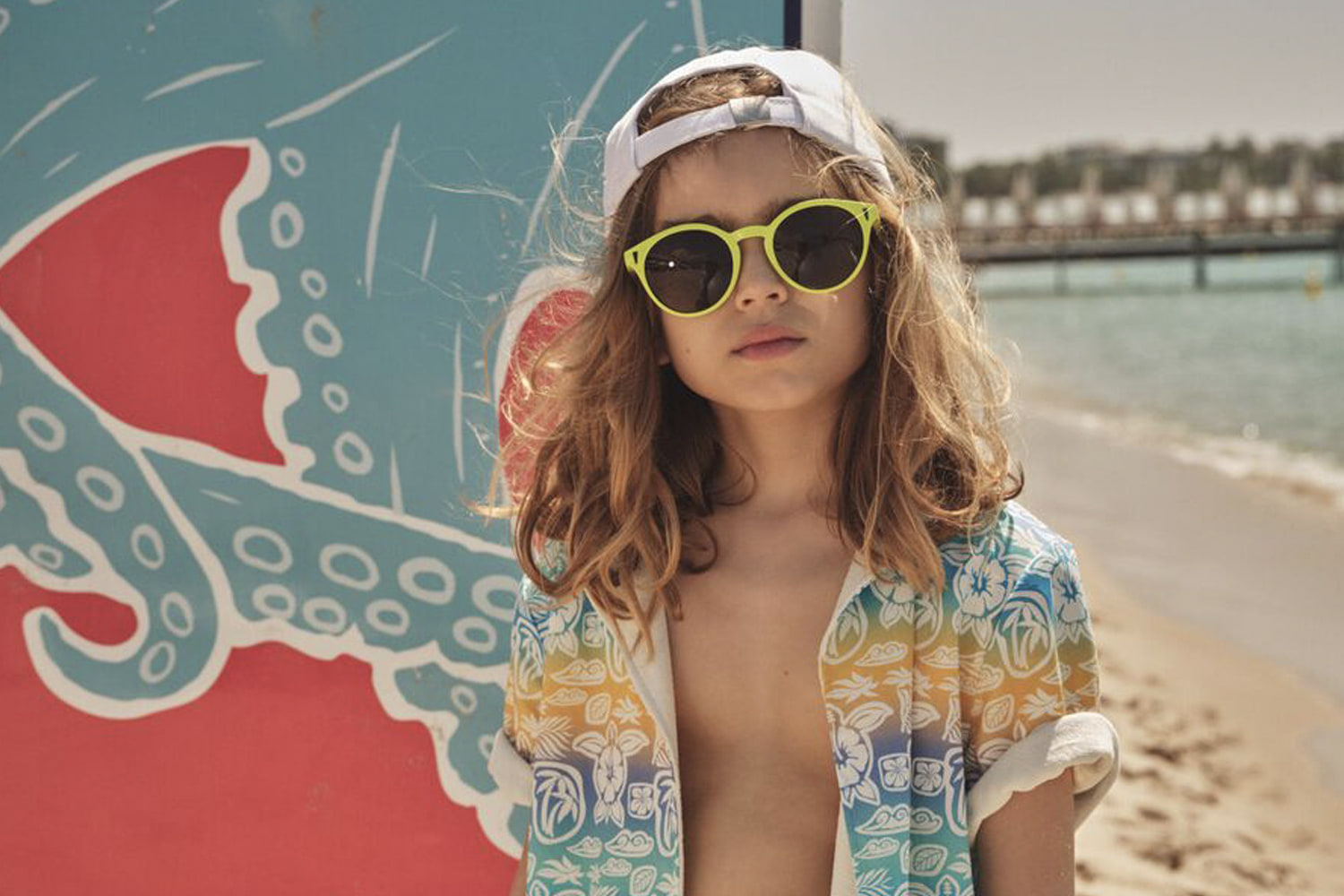 Enfant aux lunettes de soleil jaunes et chemise imprimée sur une plage